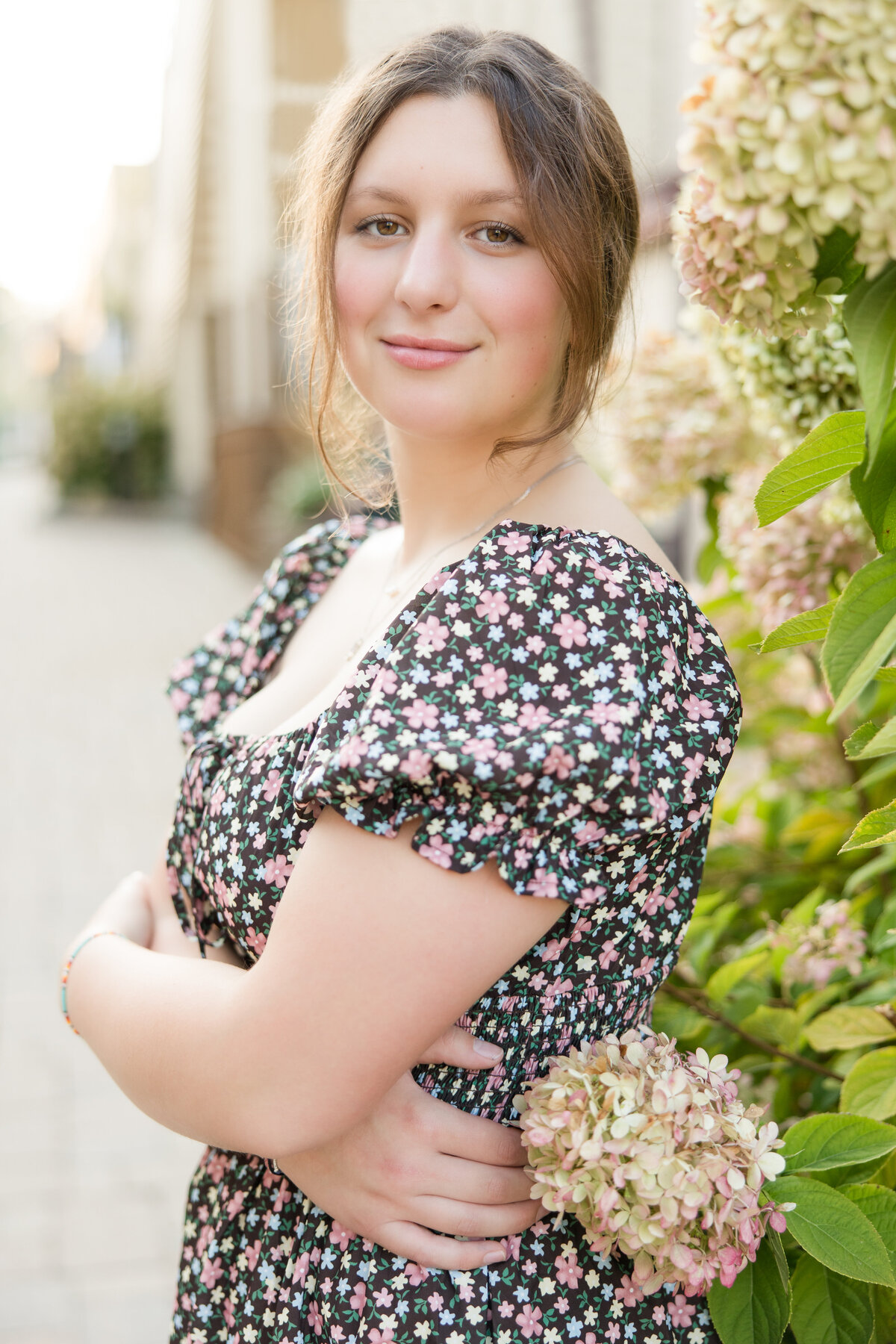 Senior girl standing in front of a flower bush smiling at the camera