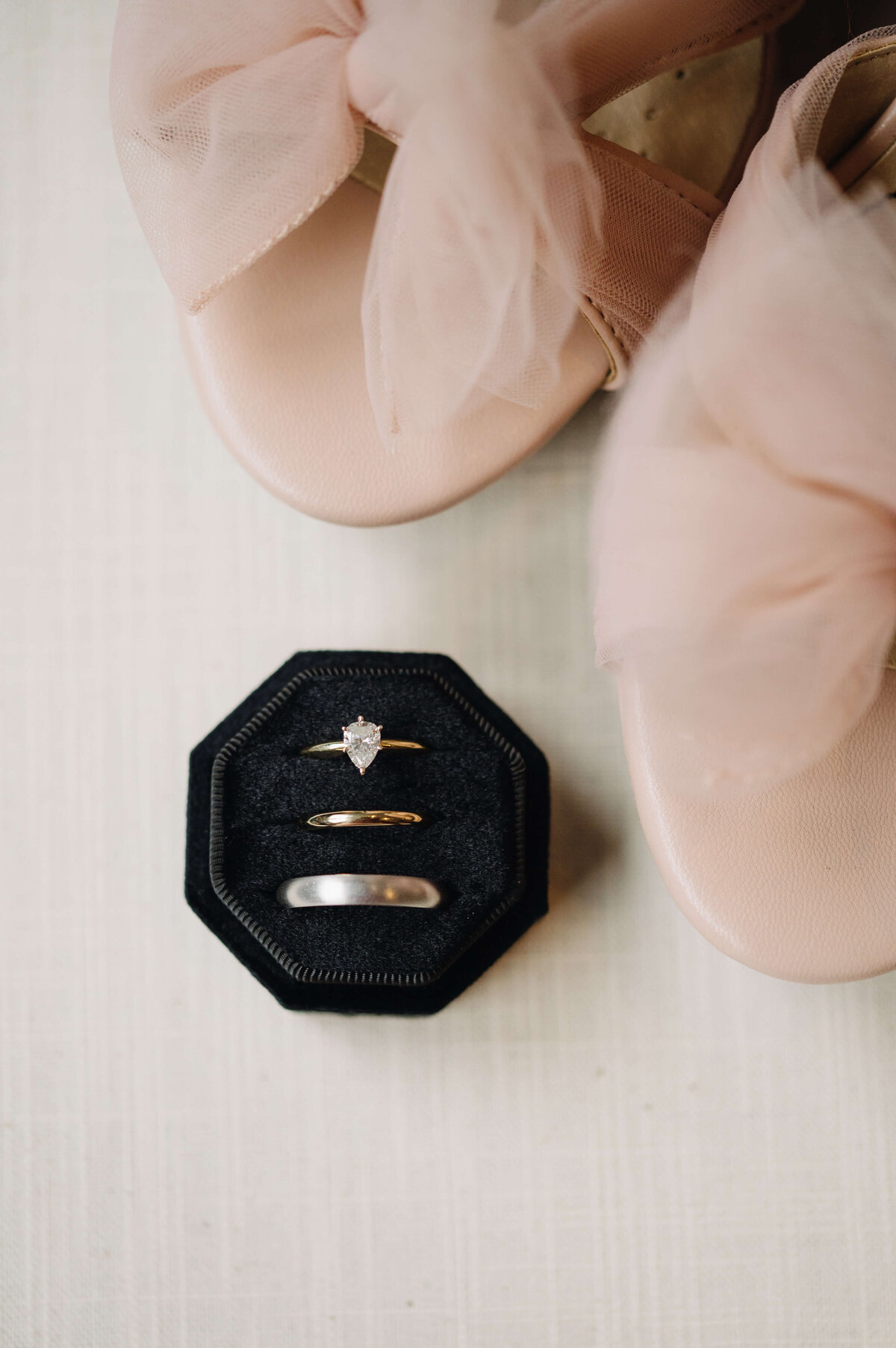 Richmond wedding photographer captures detail photo of brides wedding band and engagment ring with grooms wedding ring in a black hexagon box with the brides wedding shoes