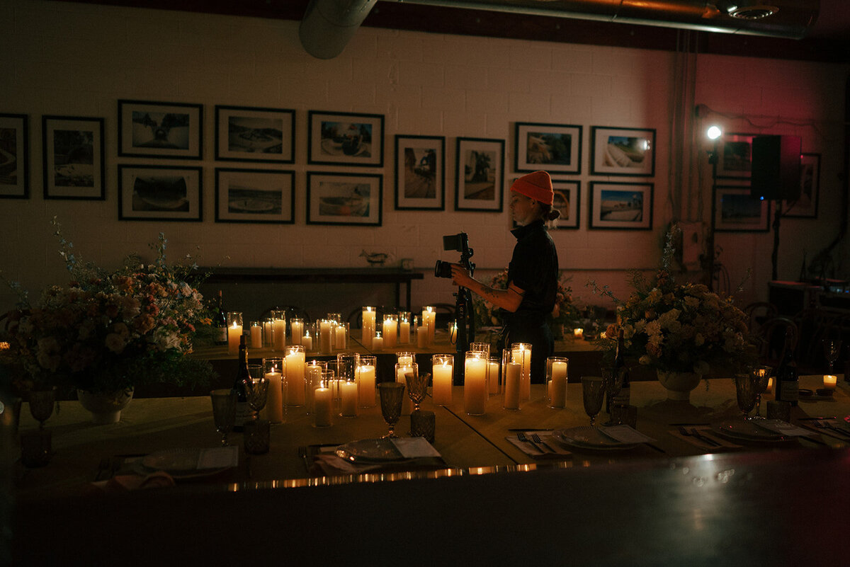 Set tables with glowing candles and a woman in the background with a camera.