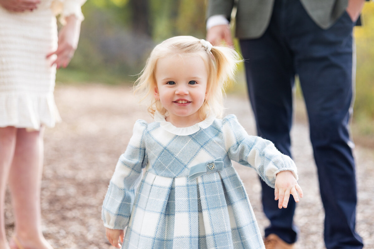 Toddler girl in a blue and white plaid dress smiles at the camera.
