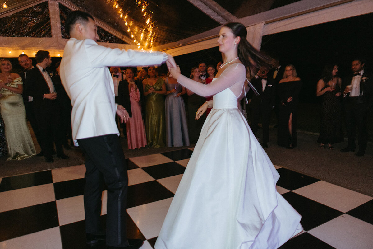 Bride spinning in silk wedding dress while groom and guests cheers her on.