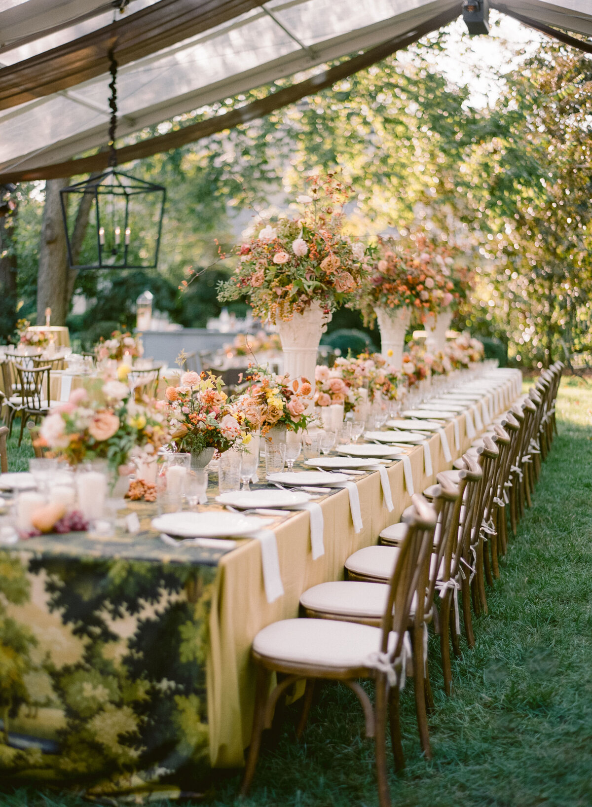 Lush fall florals for low and high centerpieces at fall wedding reception. Clear tented wedding reception in the family's back yard creating an intimate wedding reception environment. Whimsical and organic floral design in colors of copper, yellow, blush,and brown. Fall florals with sweet peas, dahlias, butterfly ranunculus, roses, mums, and bittersweet berries. Design by Rosemary & Finch Floral Design in Nashville, TN.
