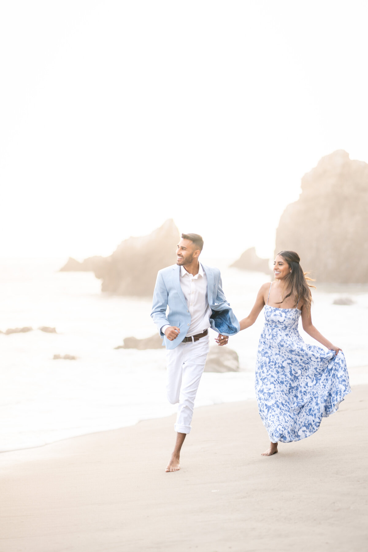 Indian couple eloping at El Matador State Beach in Malibu during low-tide sunset running on beach.