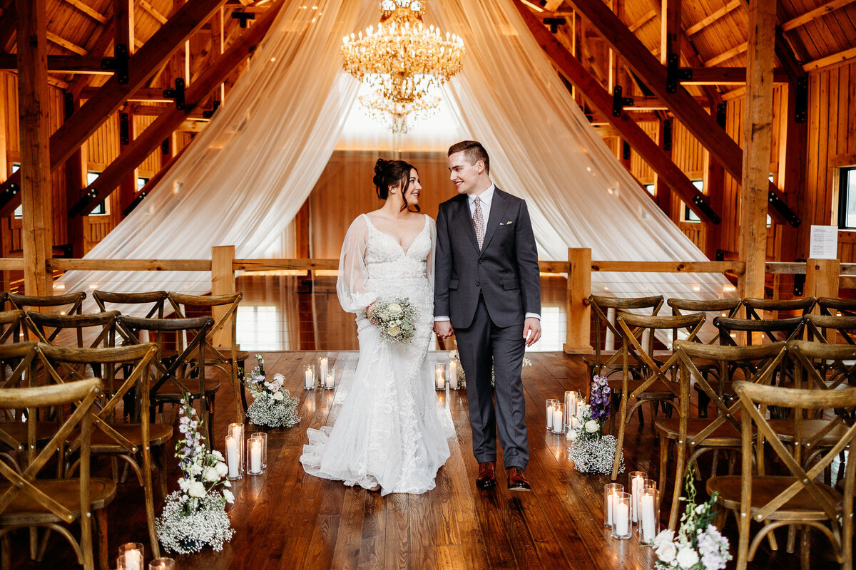 Newly wed couple stands amongst their ceremony location. The aisle lined with candles and flowers. Beautiful sheer drapes and a chandelier in the background