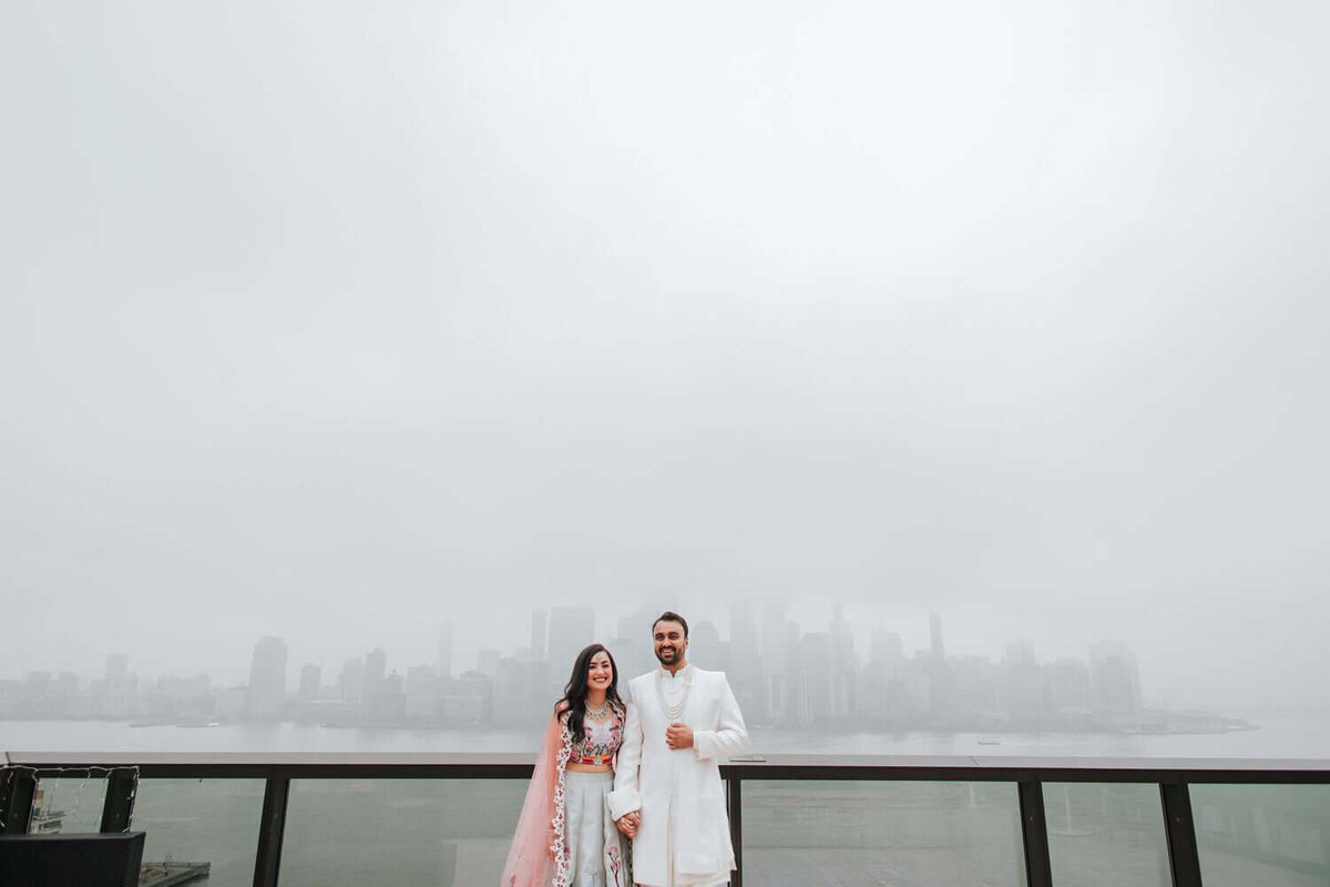 South Asian bride and groom stand on rooftop overlooking New Yorks skyline.