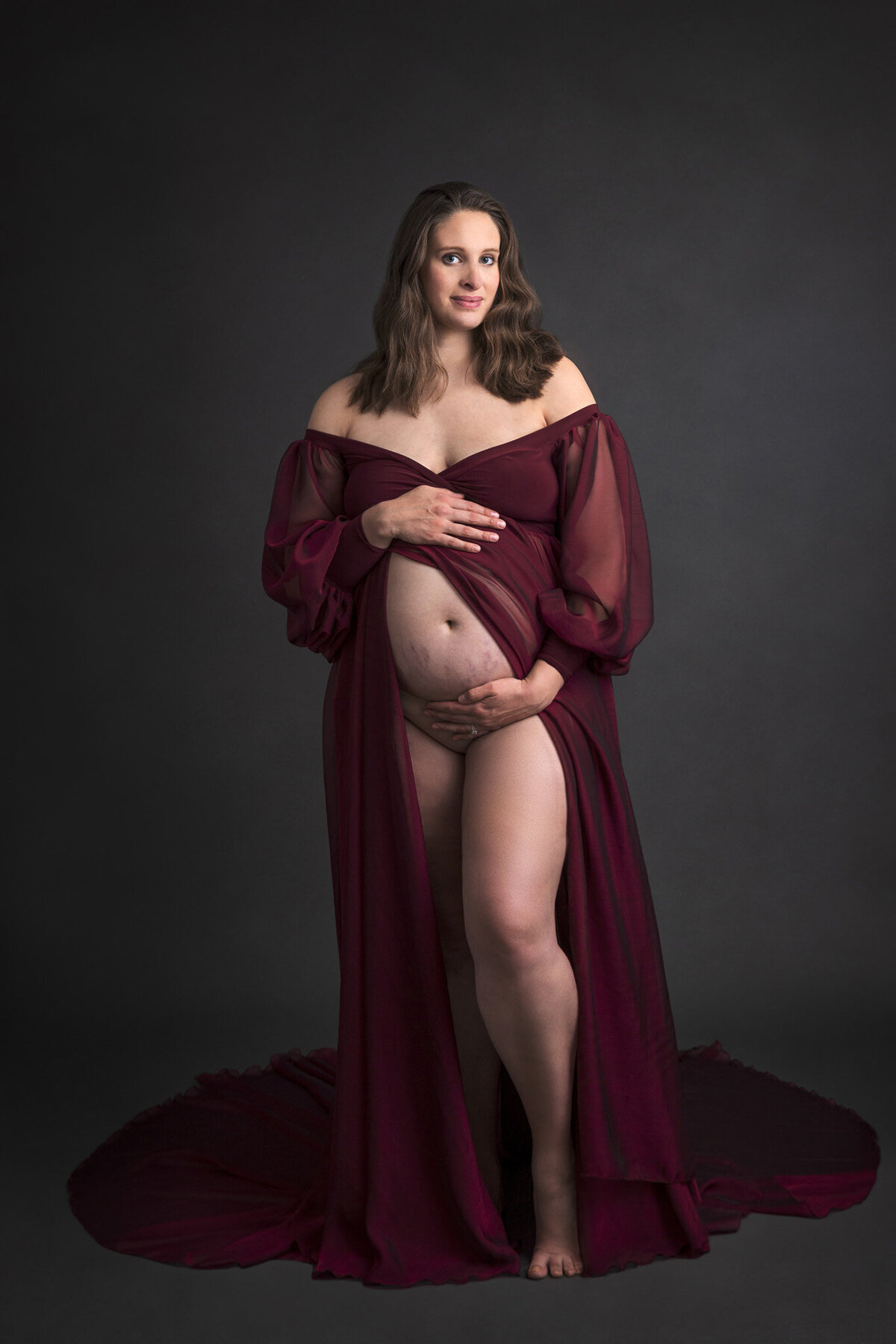 pregnant woman in a flowy maroon dress holding her belly
