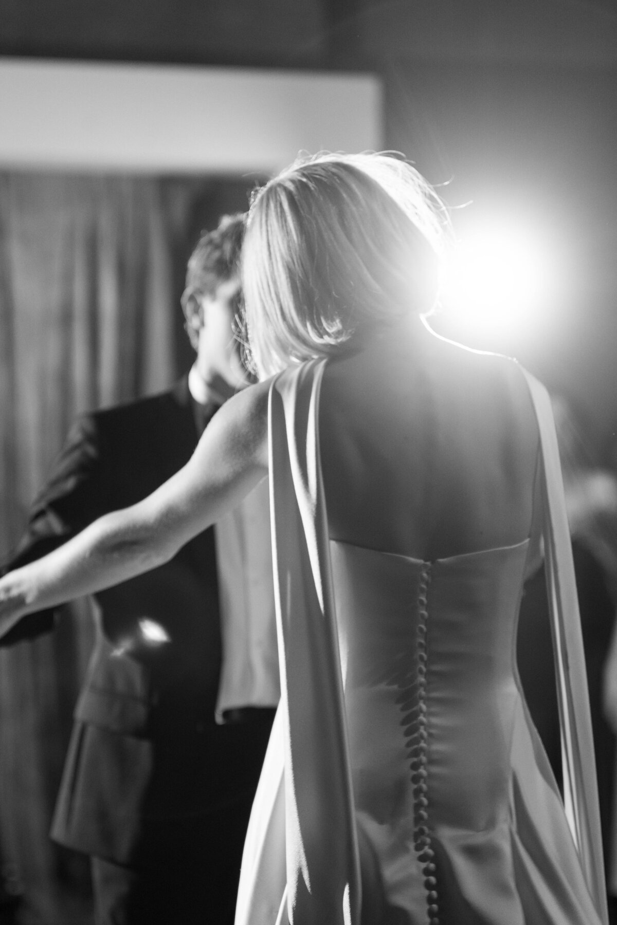 Bride dancing in backless gown with draped shoulders and dramatic lighting