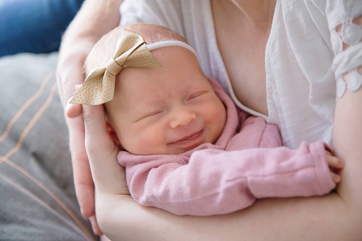 smiling newborn baby girl snuggled in mother's arms during their newborn photography session