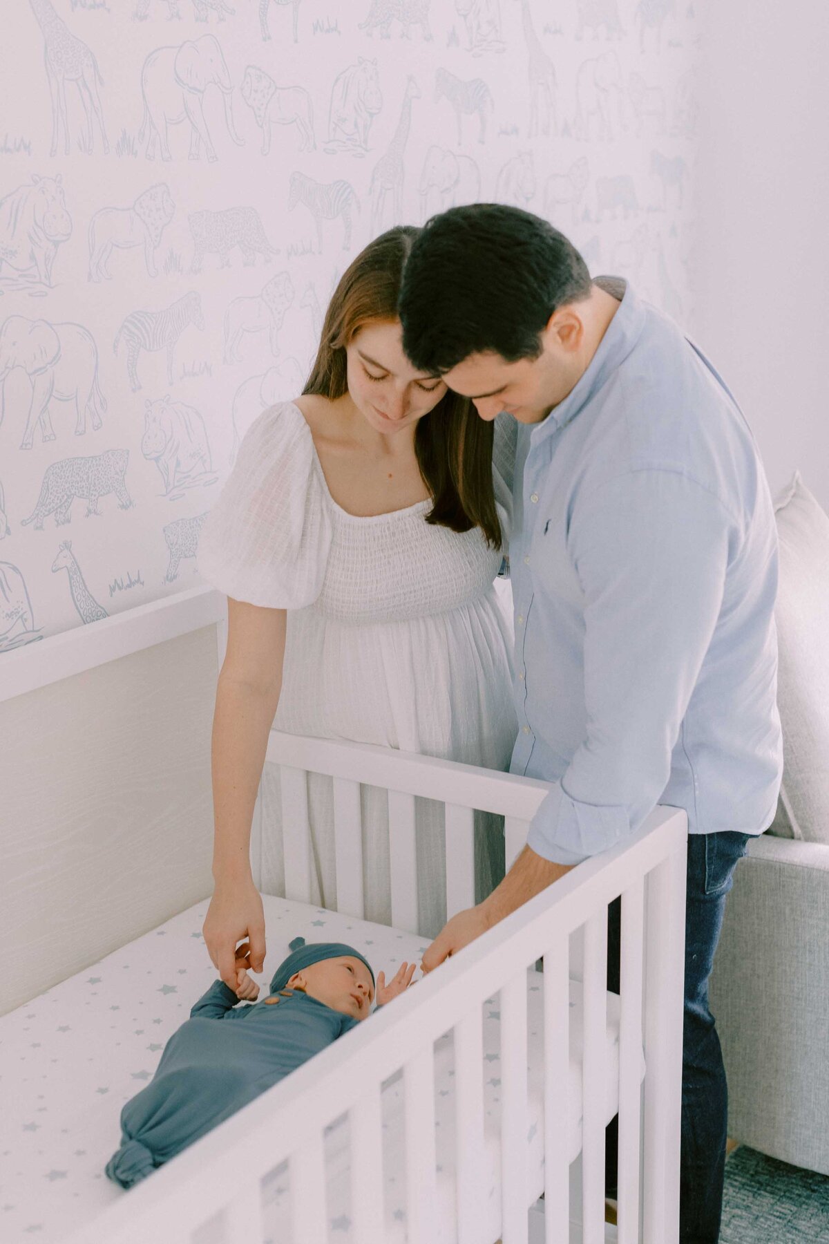 Baby laying in crib while parents hold both of his hands