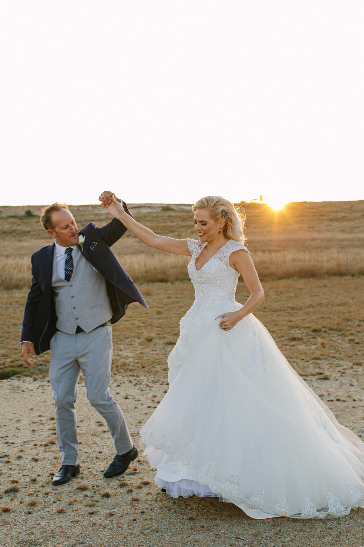 Candid moment of the couple twirling and laughing on the salt pans, with the golden sunset behind them.