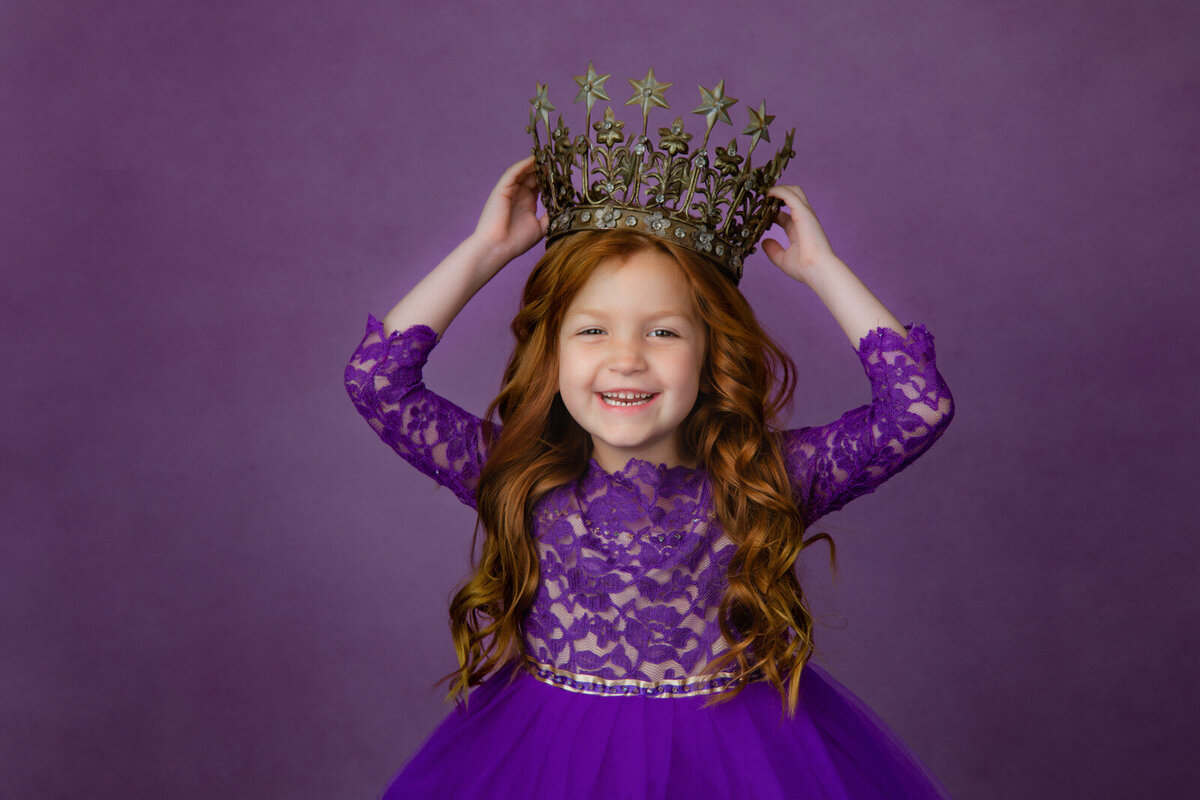 girl-in-purple-lace-dress-against-a-purple-backdrop-in-studio-arlington-tx-holding-crown