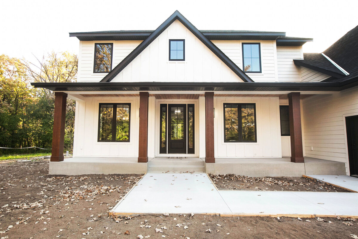 Exterior view of custom home in Big Lake Township, Minnesota with farmhouse details, cream siding, wood pillars and front porch built by Cornerstone Custom Builds