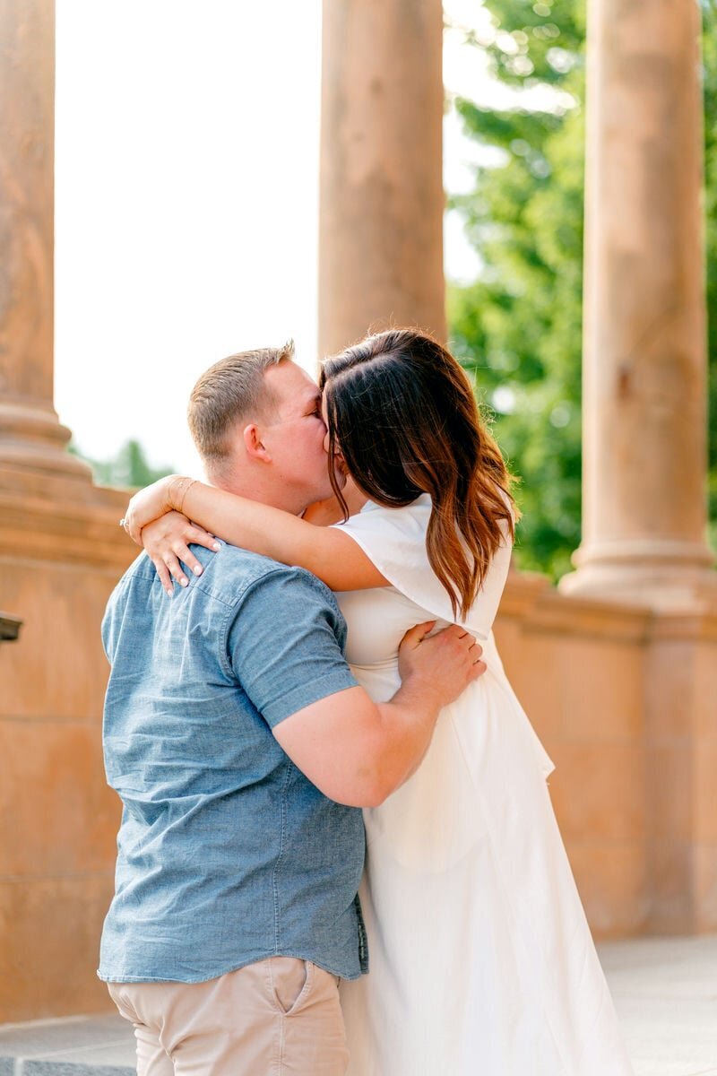 Couple kissing in front of stone columns during their engagement photo session, capturing a moment of love and intimacy.