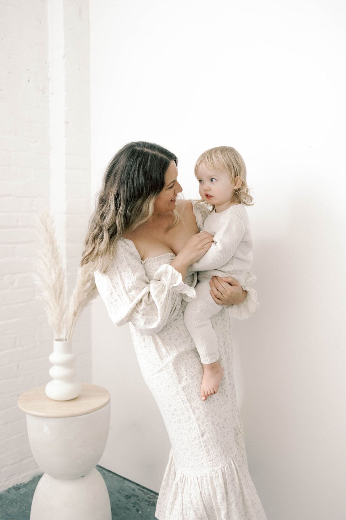 Mother holds baby smiling in white room.