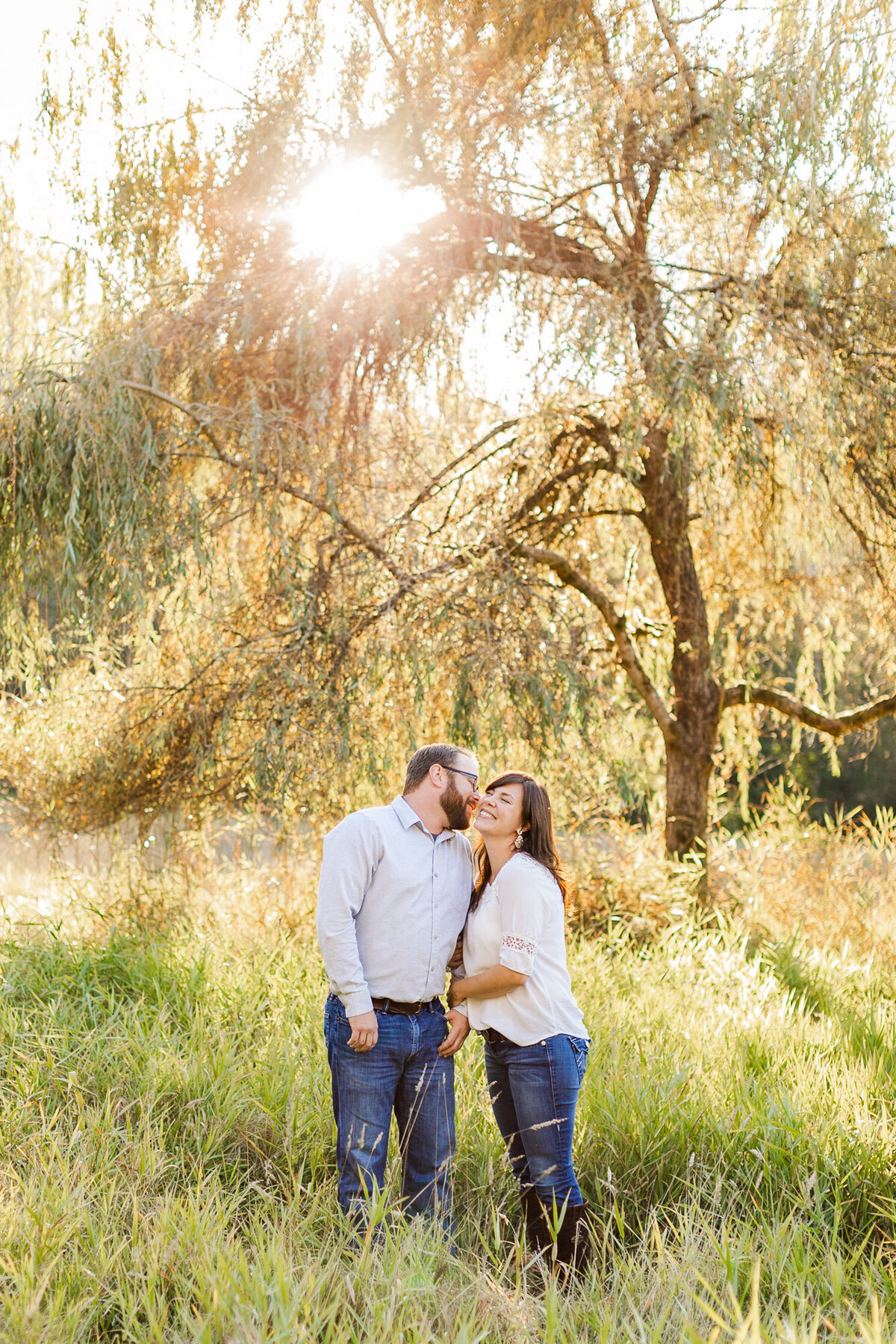 Beautiful golden hour engagement session in field in Woodiville WA willow tree happy couple laughing colorful candid photo by Joanna Monger Photography