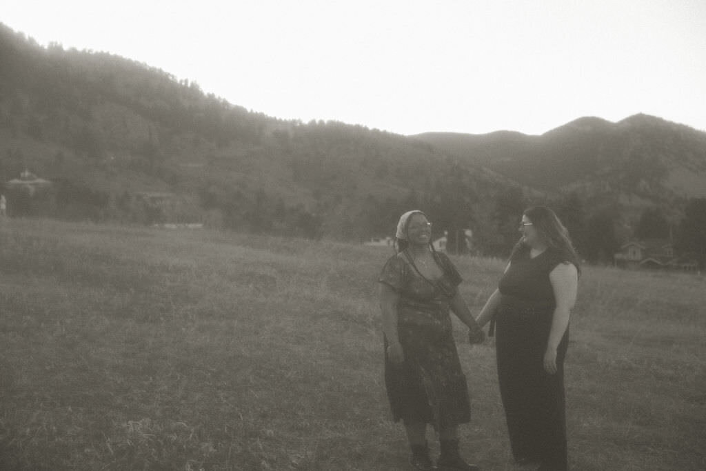 A couple holding hands and walking in a field at sunset.