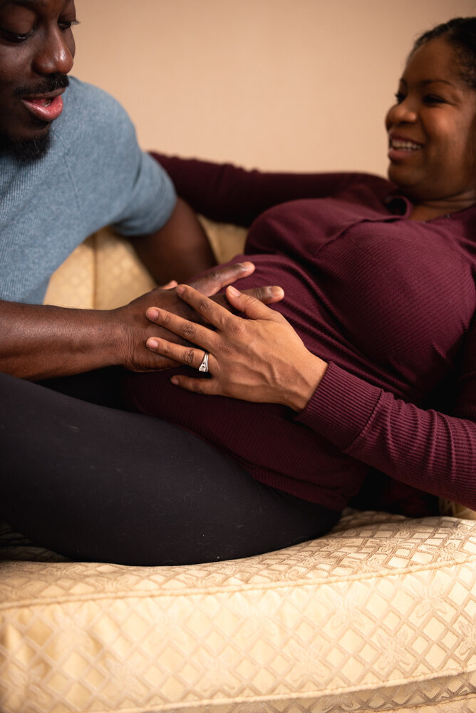 Up close photo of husband holding wife's hand, both resting on their baby growing inside mom's belly
