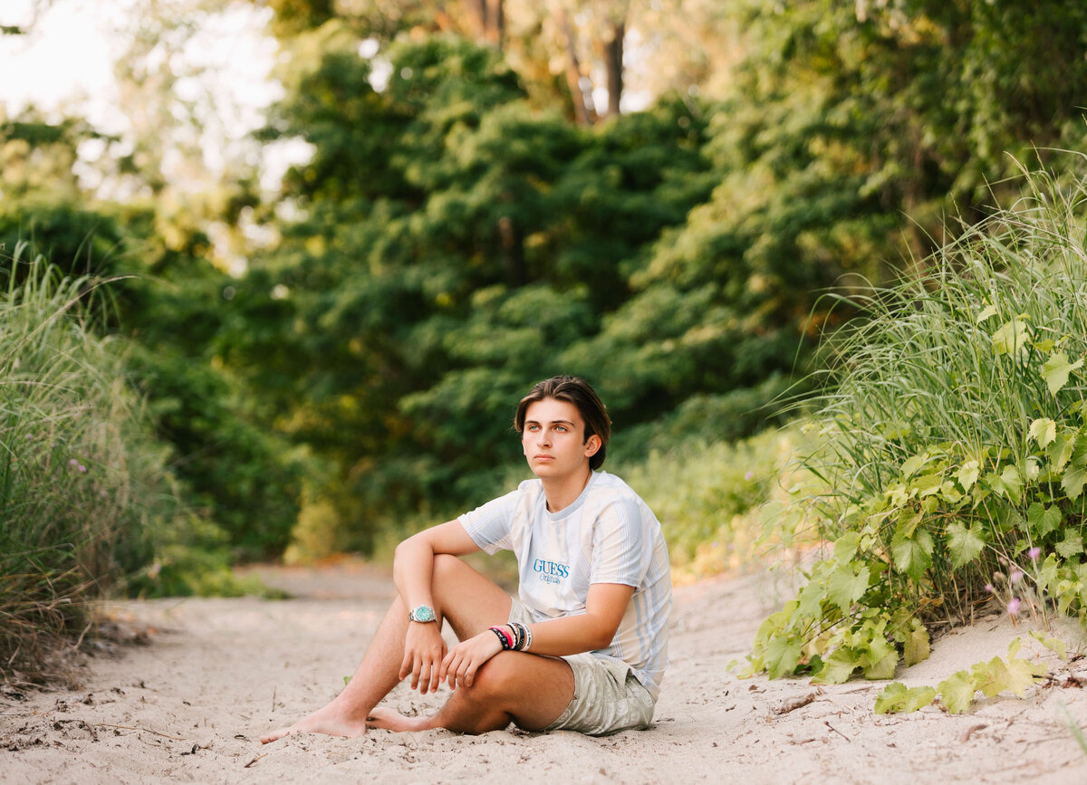 Senior portrait of a boy sitting in the sand at an Erie Pa beach