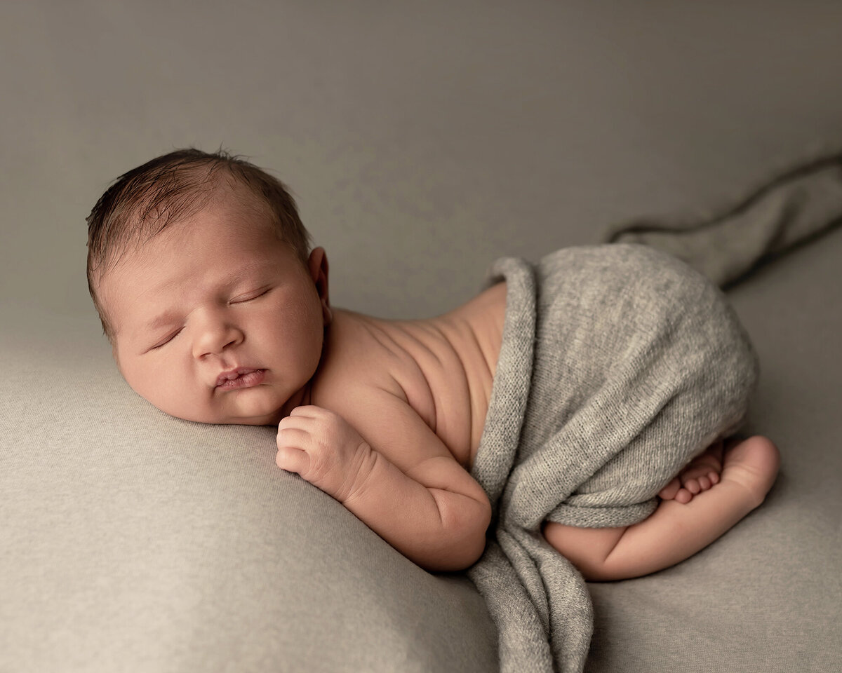 A newborn lays in froggy pose under grey blanket