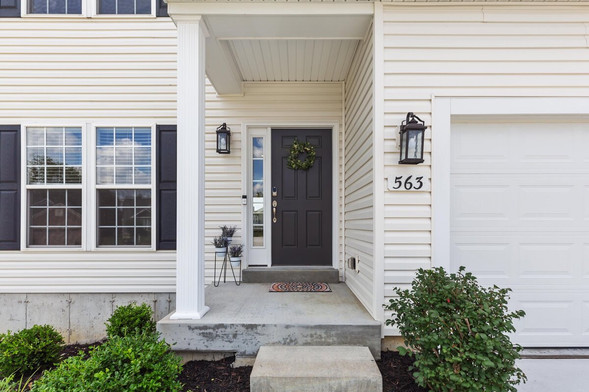 Front porch of a home with white siding, black shutters, and a black door.