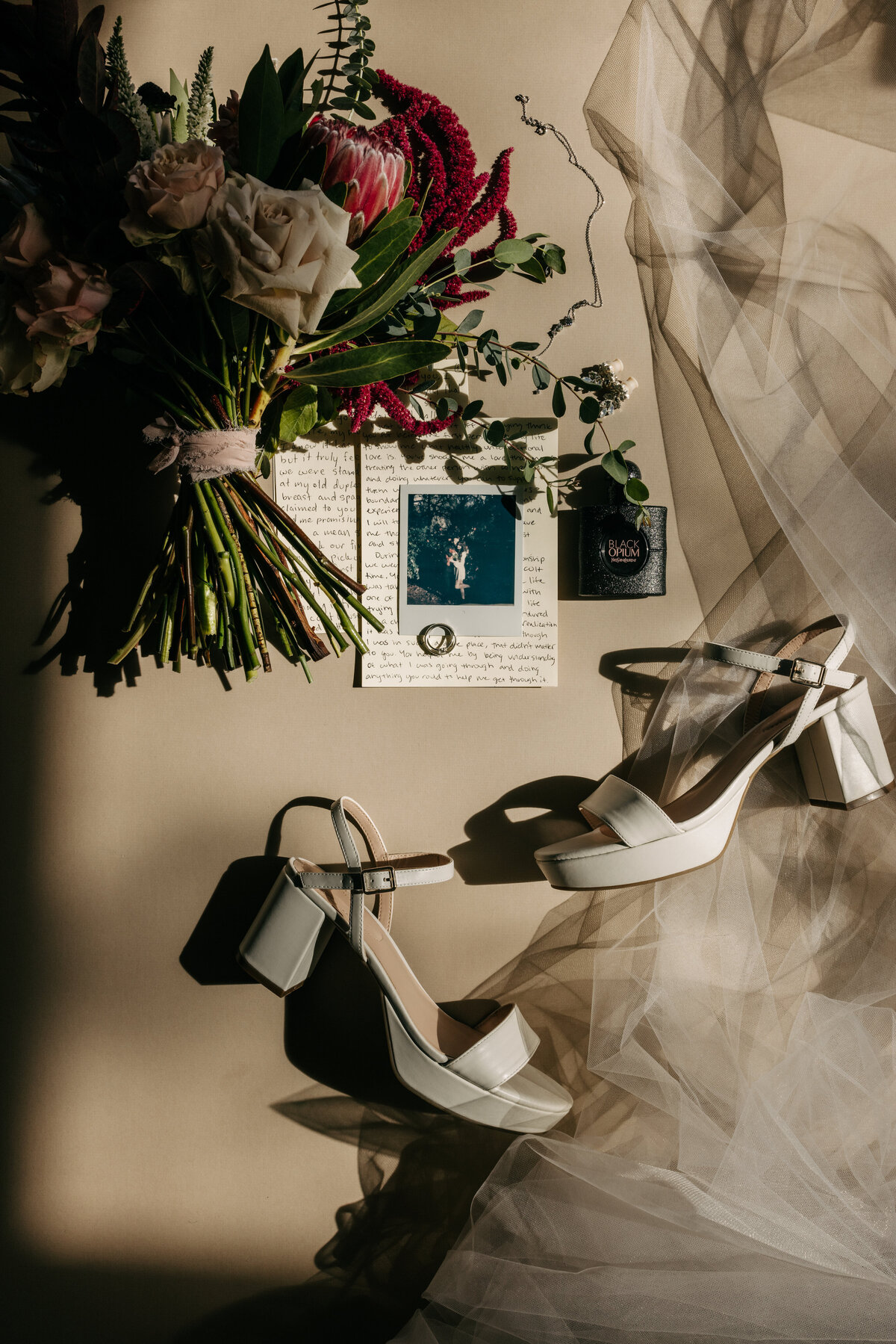 pink florals polaroid perfume gauge wedding earrings platform shoes and viel wedding details shot in direct sunlight flatlay