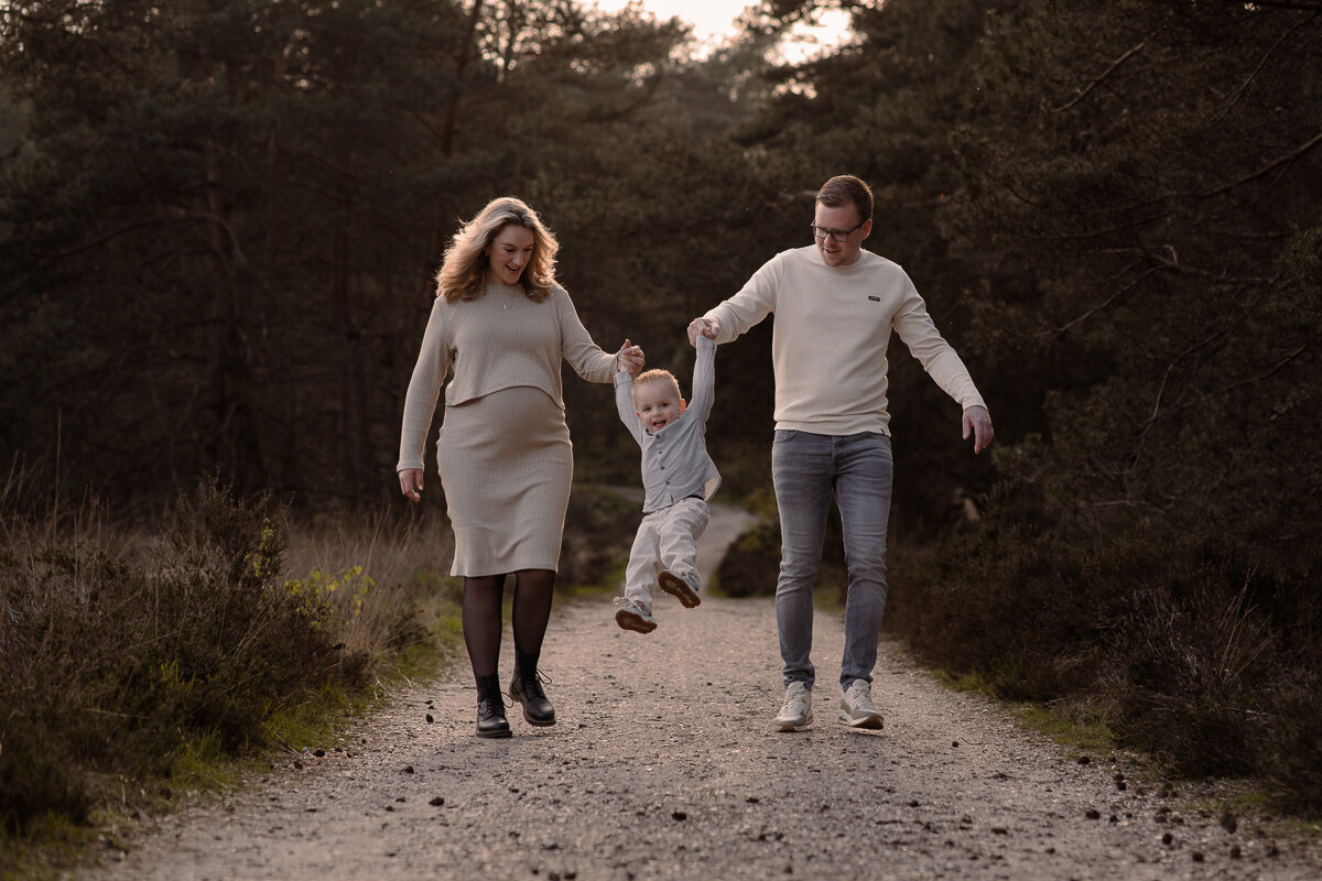 Zwangere moeder en vader slinger hun zoontje met de handen naar voren tijdens het wandelen