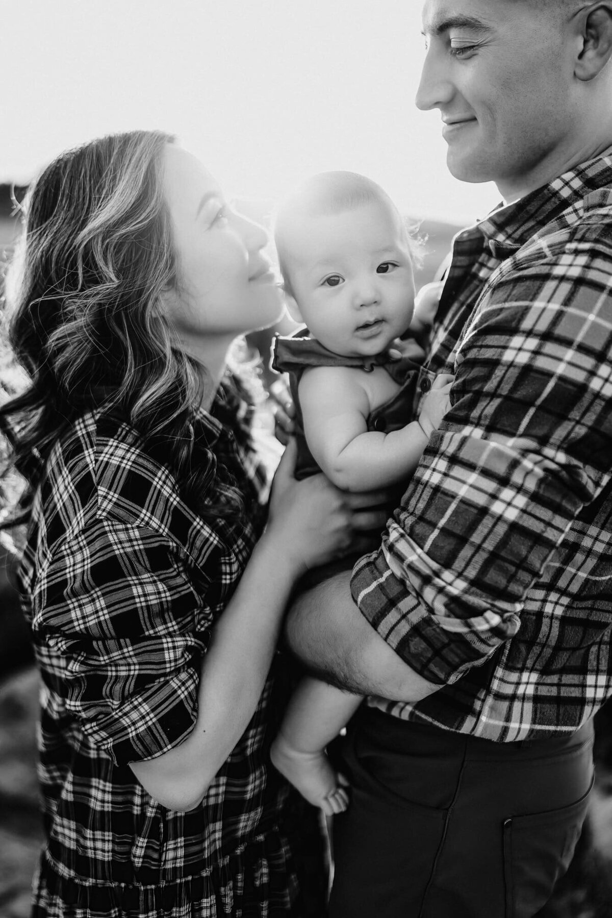 A man and woman look at each other and smile, holding their baby between them, during a San Diego  lifestyle family photo session by Love Michelle Photography