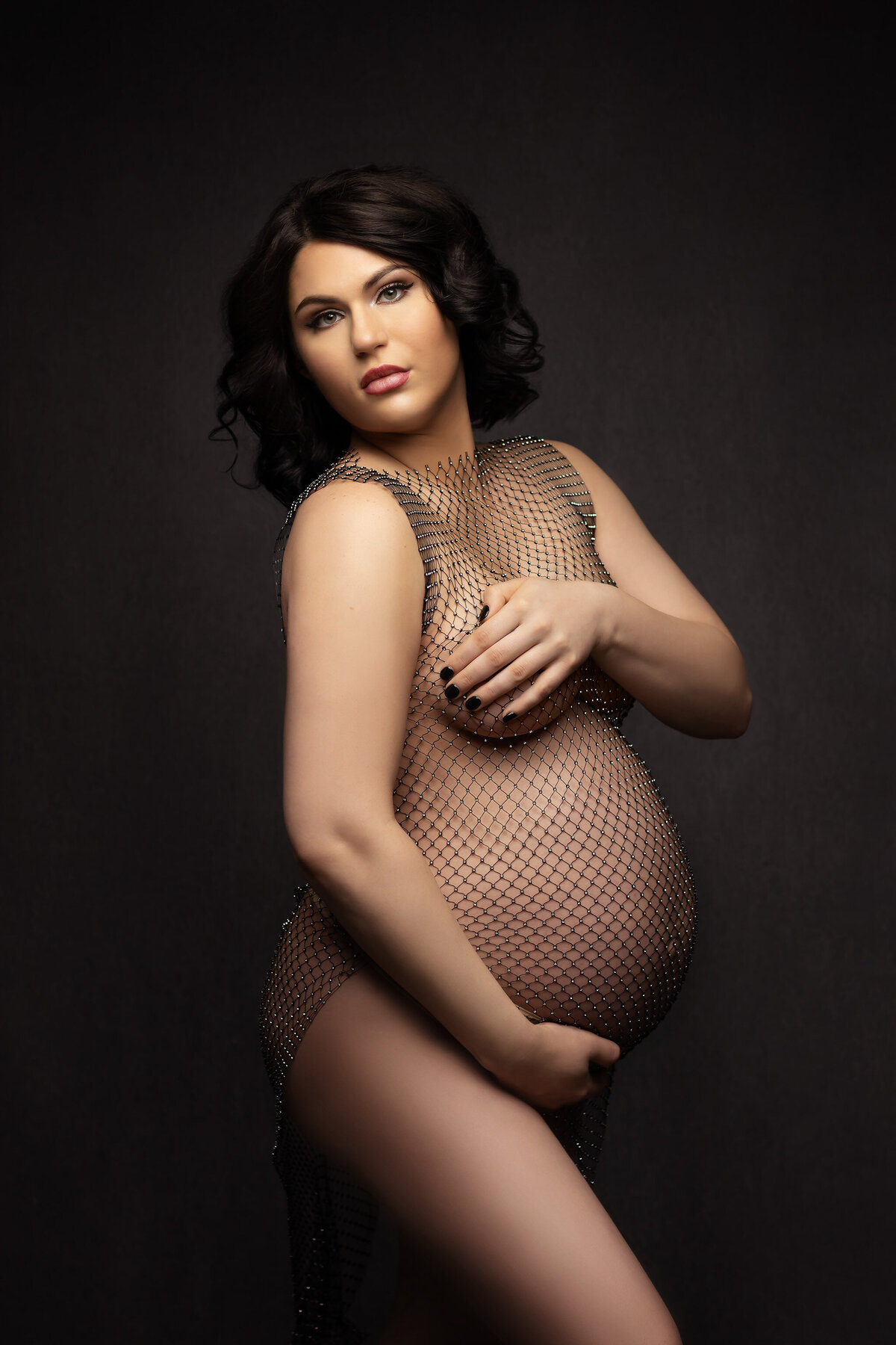 Dallas maternity photographer captures woman in shimmering mesh drape against dark backdrop. Captured by Lindsay Walden Photography.
