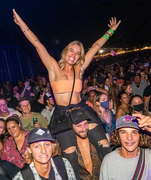 Young woman with arms raised on shoulders in a packed night crowd at St Kilda Festival live concert