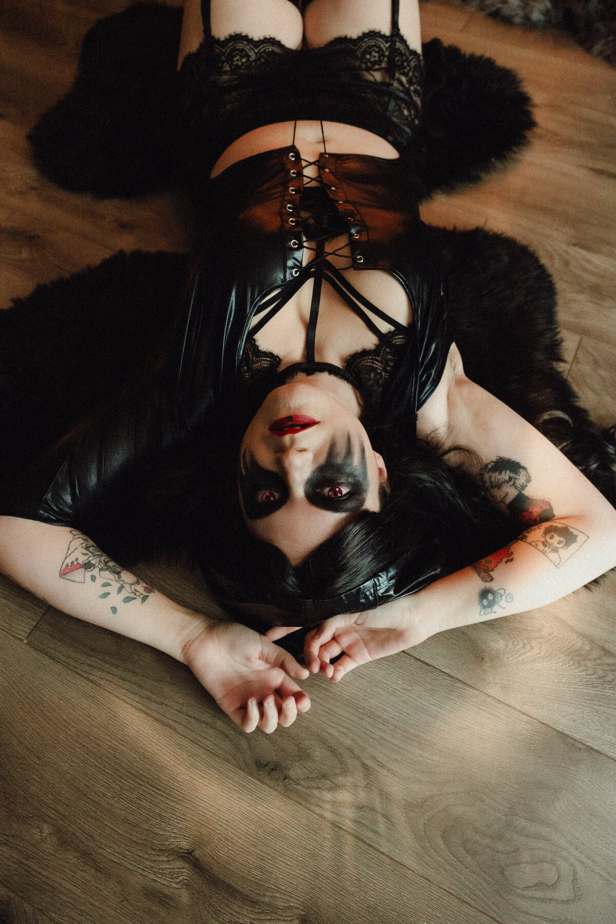 Woman in black leather and lace lingerie poses on the floor with dramatic dark eye makeup during a conceptual boudoir shoot in Orlando.