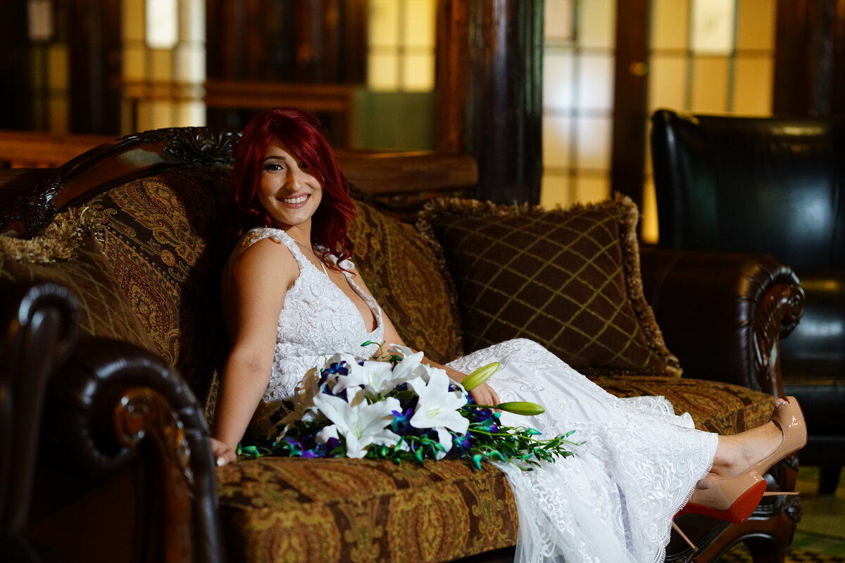 A smiling bride lies gracefully on a sofa, showcasing her elegant wedding attire and relaxed demeanor. This image captures a serene and intimate moment in her bridal portrait session, highlighting both her joy and the sophisticated style of our wedding photography.