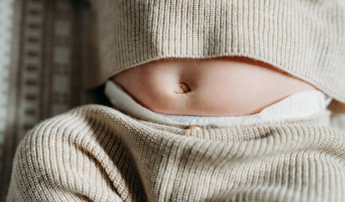 Newborn Photographer, a baby's belly button is exposed as belly pops out of knit pajamas