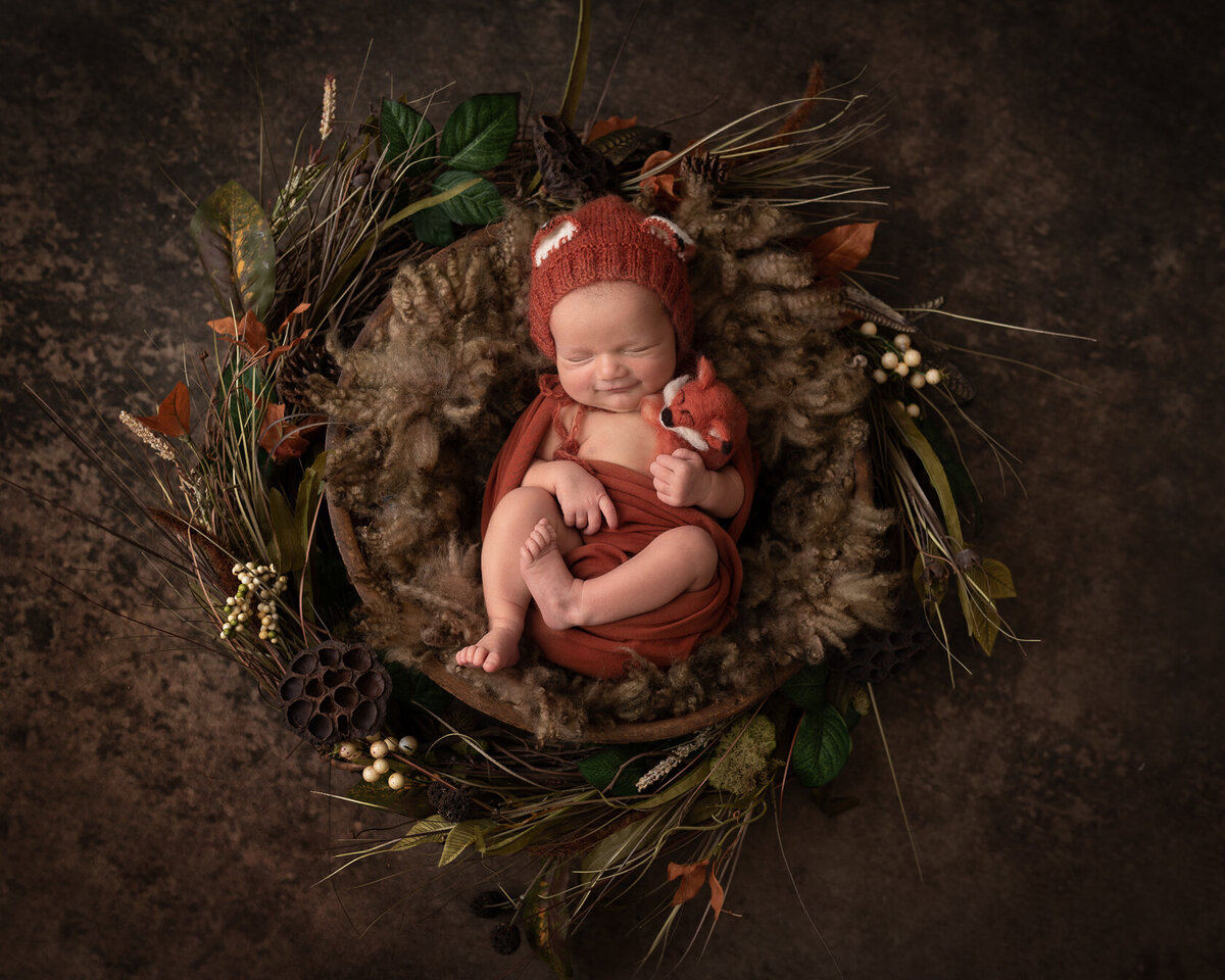 Newborn in red  knitted bonnet in creative bucket