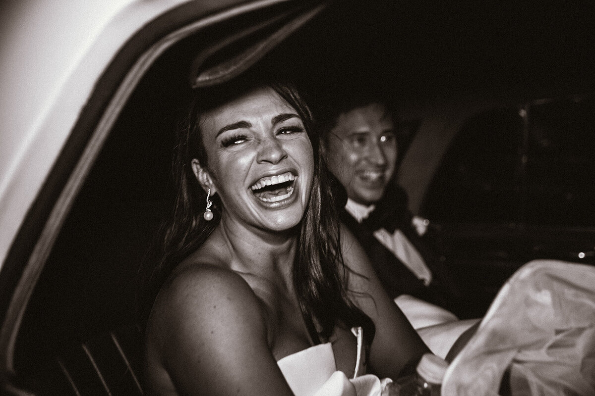 black and white photo of bride laughing in car