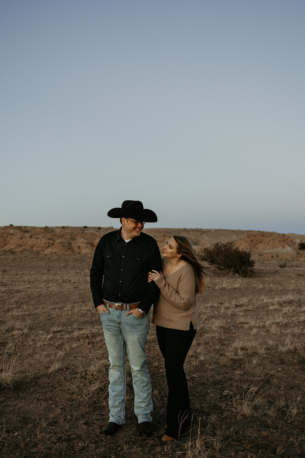 woman holding her fiancés arm looking at each other in the desert