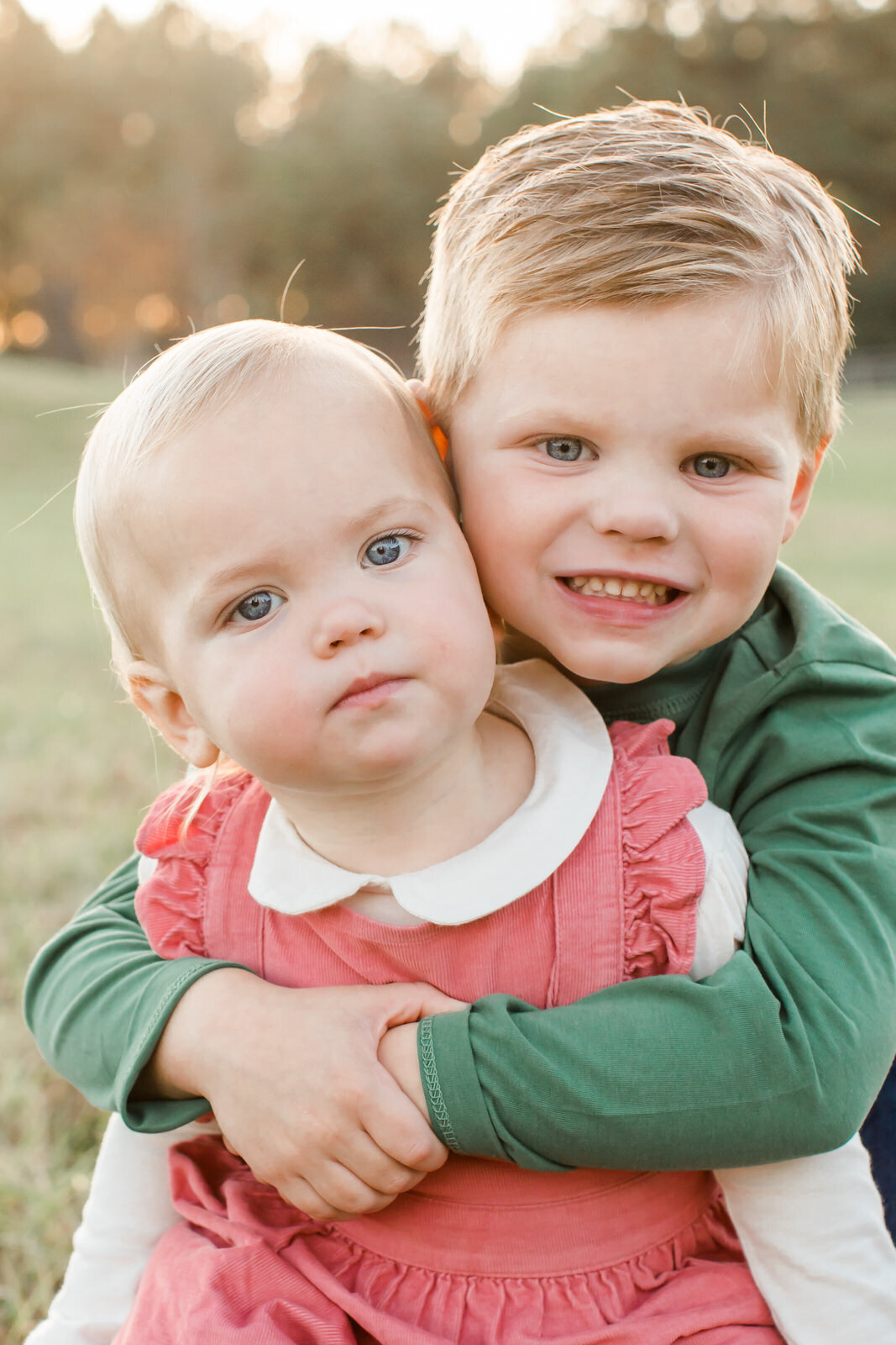 A brother hugs his little sister from behind at an extended family session