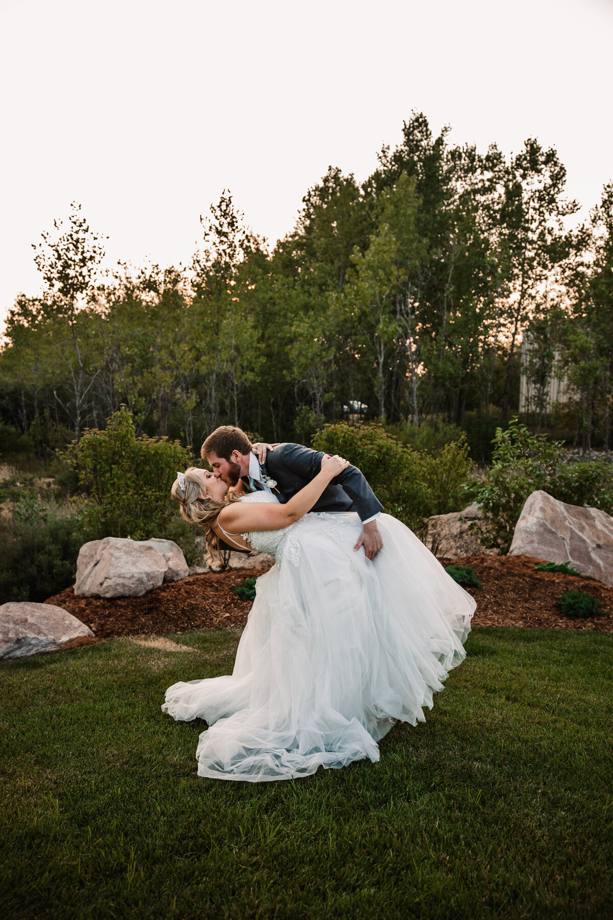 groom dips bride in grassy area while kissing
