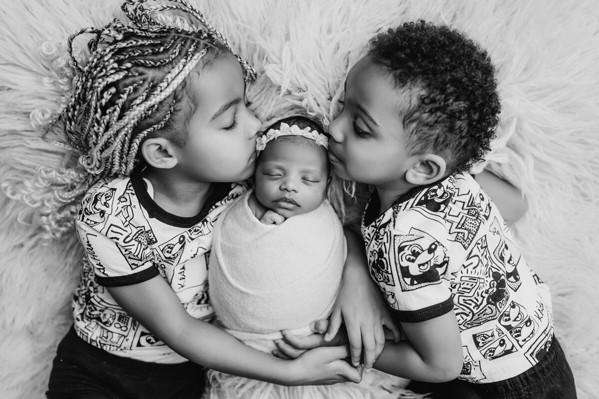 Brother and sister laying next to newborn sister kissing her head