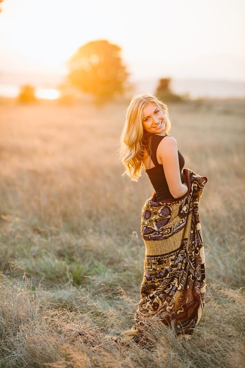 Young woman standing at a open field at sunset.