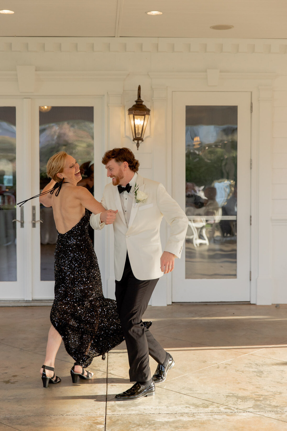 A groom dances with his mom at his wedding reception. They're country dancing in front of simple, yet beautiful white house.