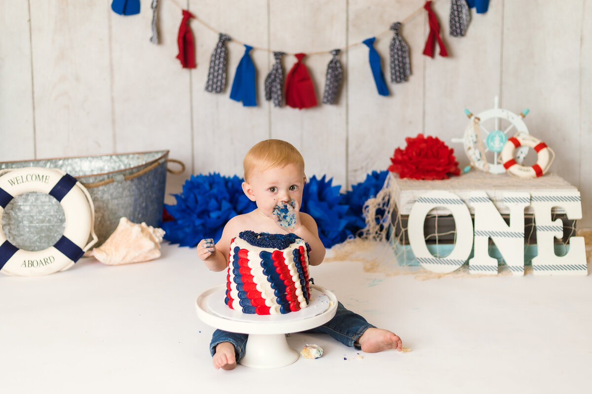 Cake Smash Photographer, a baby eats from a red, white, and blue cake