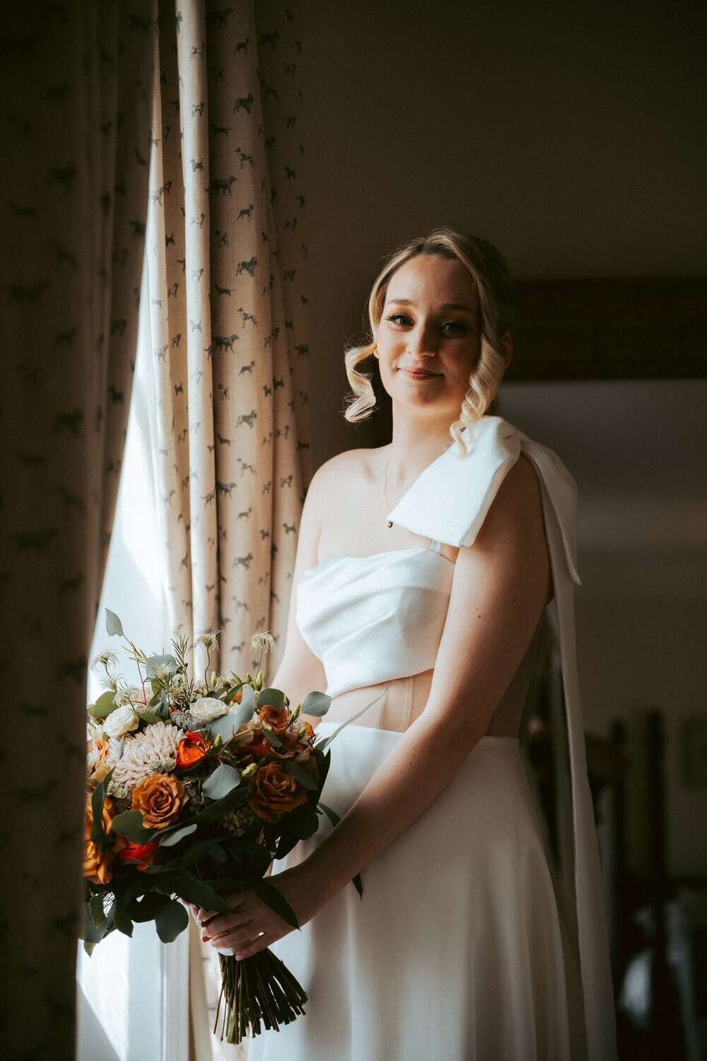 Bride stands in front of window ready and holding bouquet of flowers