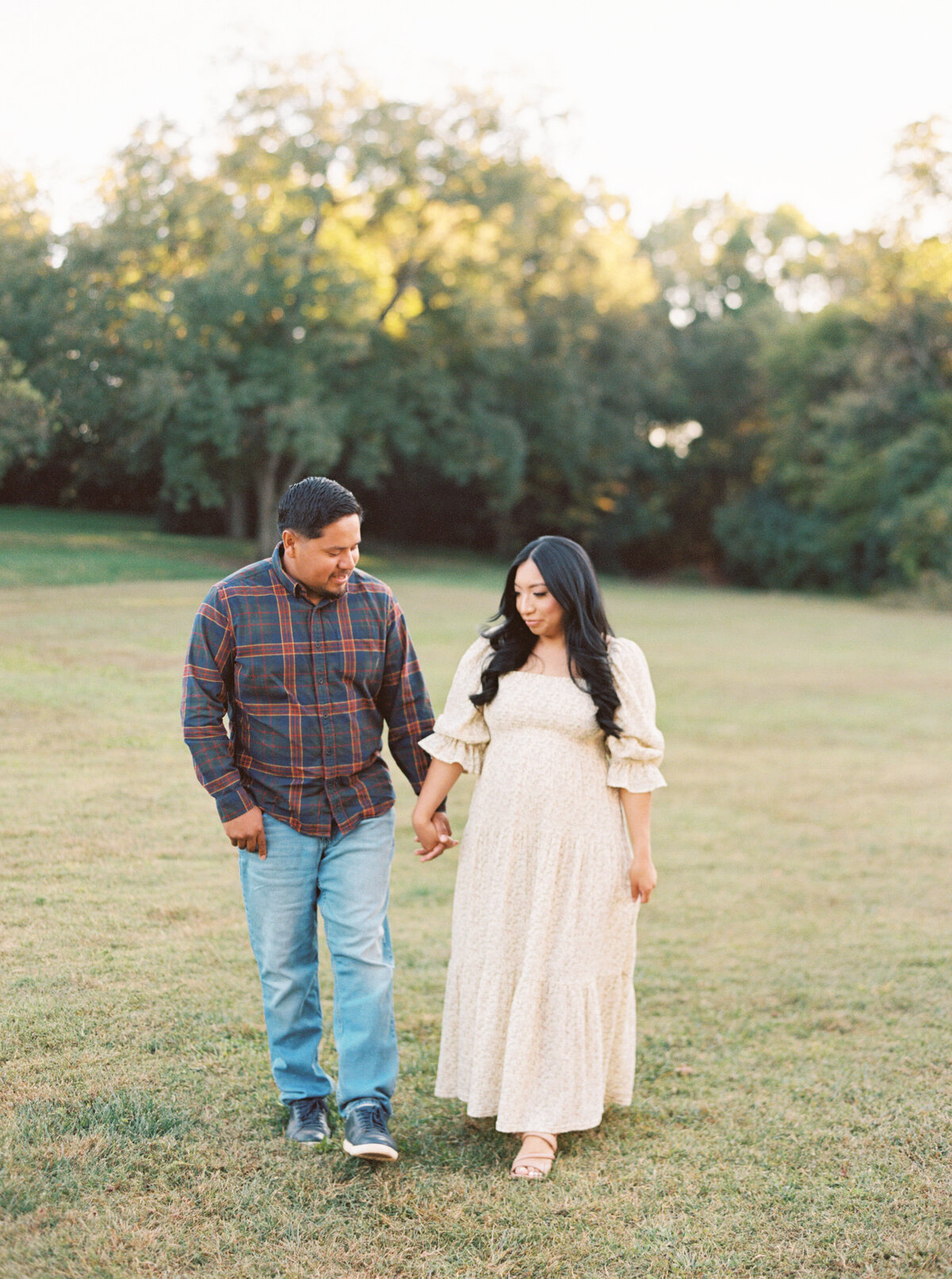 Parents walk through the field holding hands during their maternity session. Image by Raleigh maternity photographer A.J. Dunlap Photography.