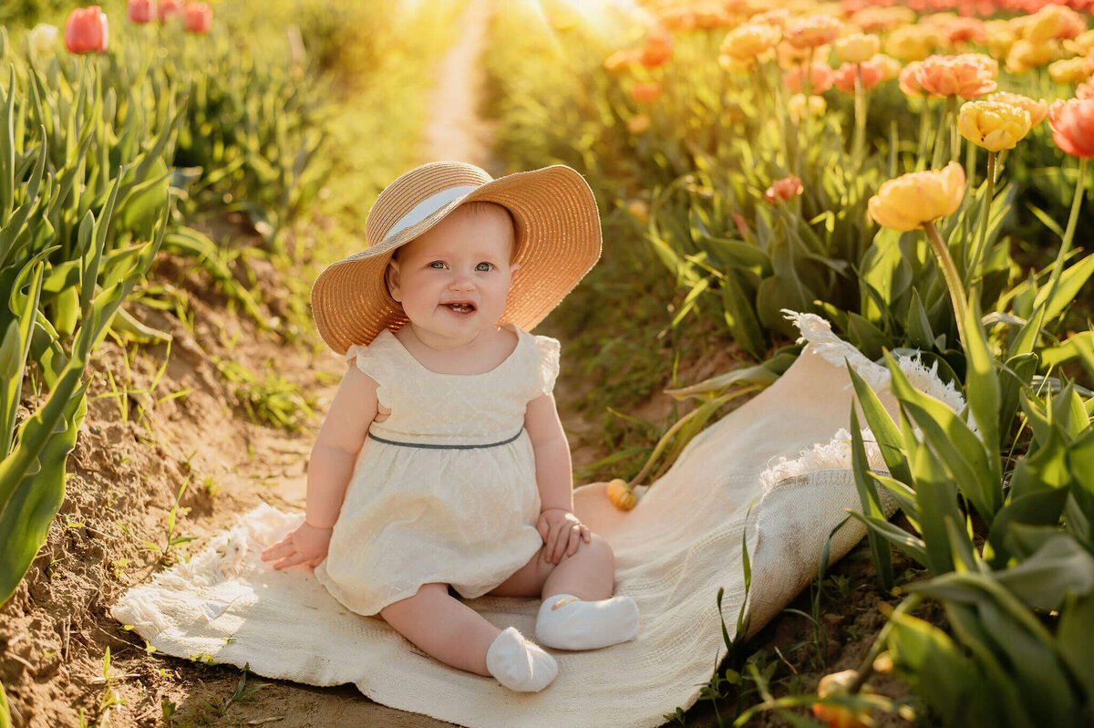 Smiling baby girl sitting between a row of multi coloured tulips at TASC farm at GTA and  Hamilton Family Photography session.