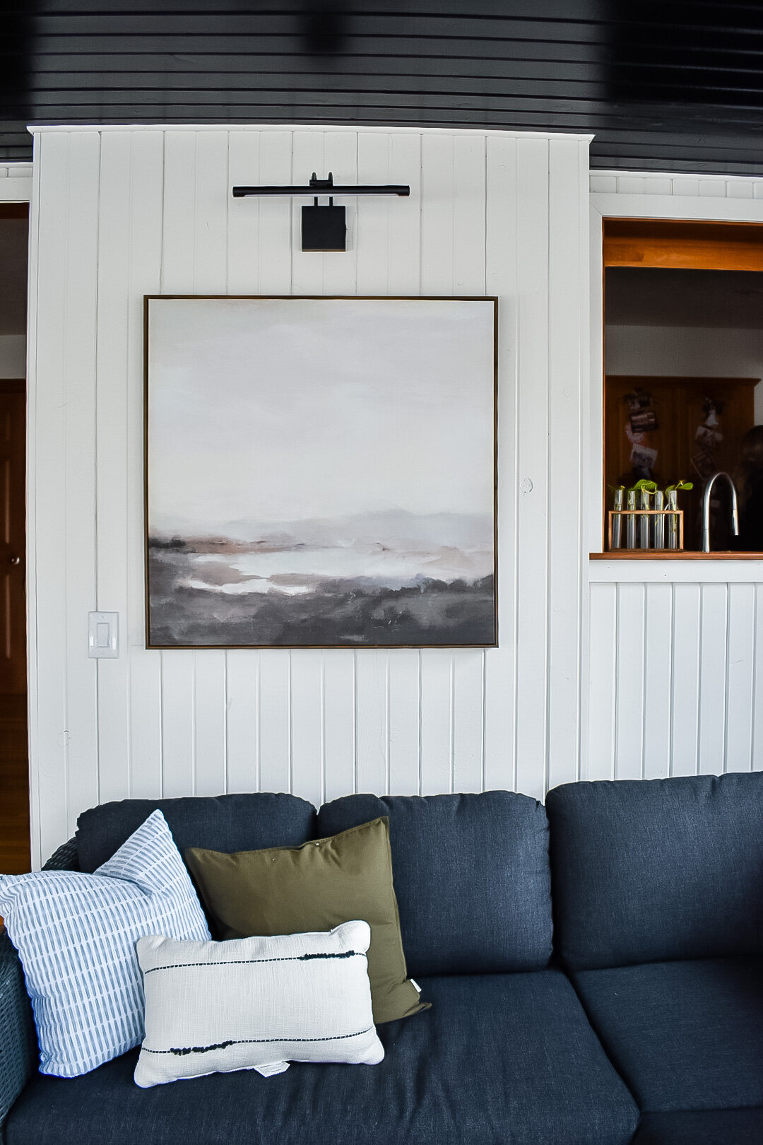 A landscape art piece hangs on a white wall with vertical panelling
