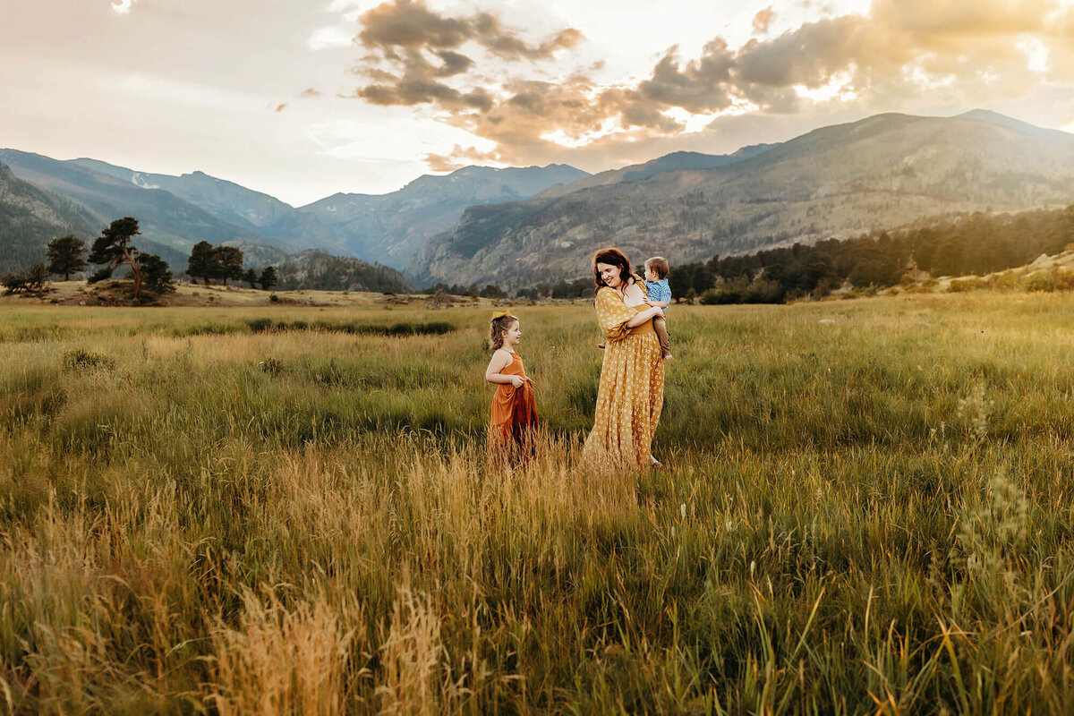 Mom carrying toddler son and smiling back at daughter in the estes park mountains.