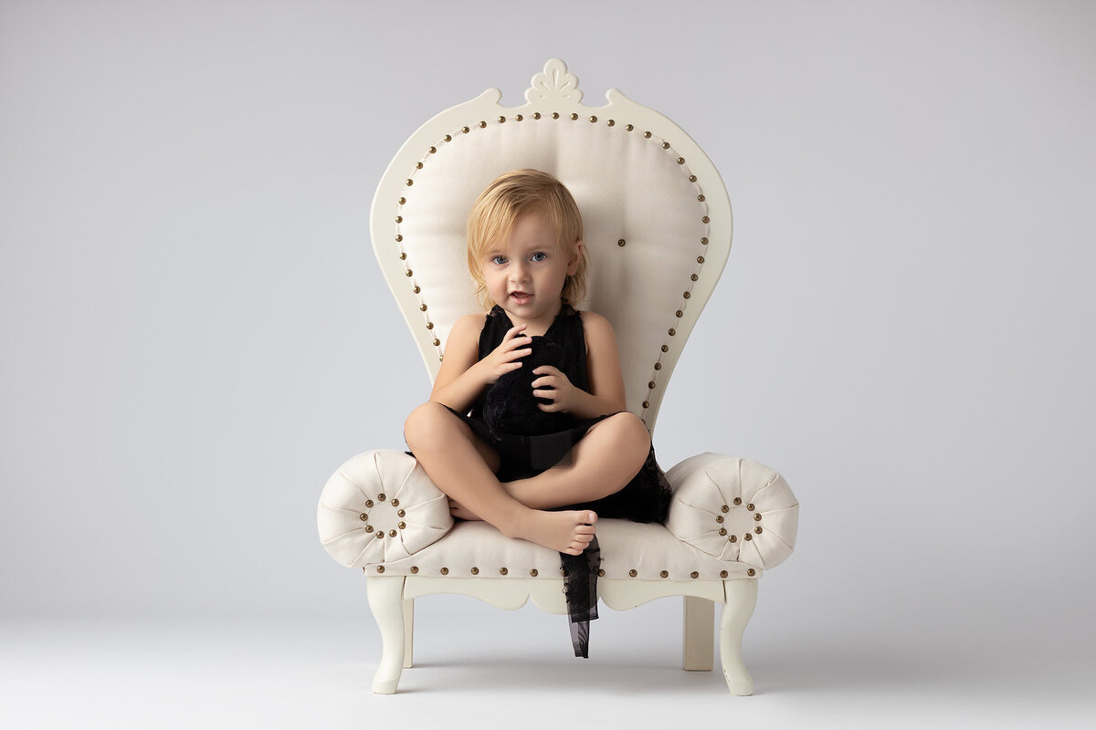 Young girl sitting on an elegant chair in Dallas family photography, exuding confidence in a black dress.