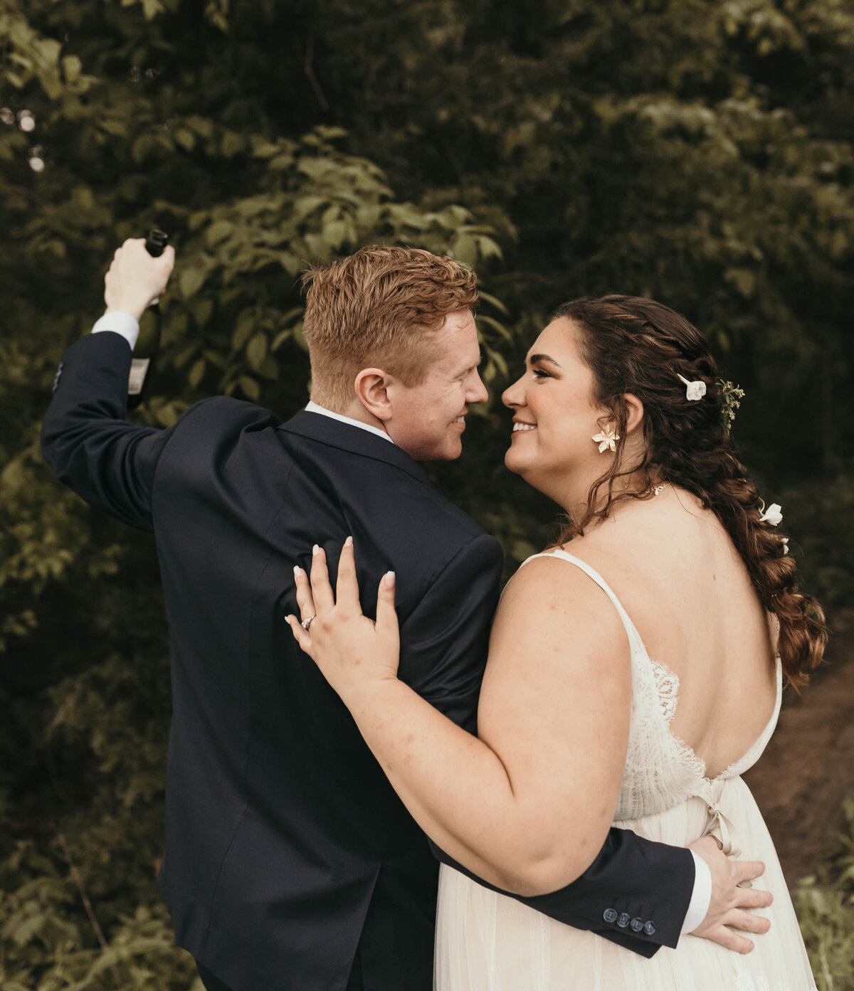 couple holding each other close, lifting up a champagne bottle in celebration