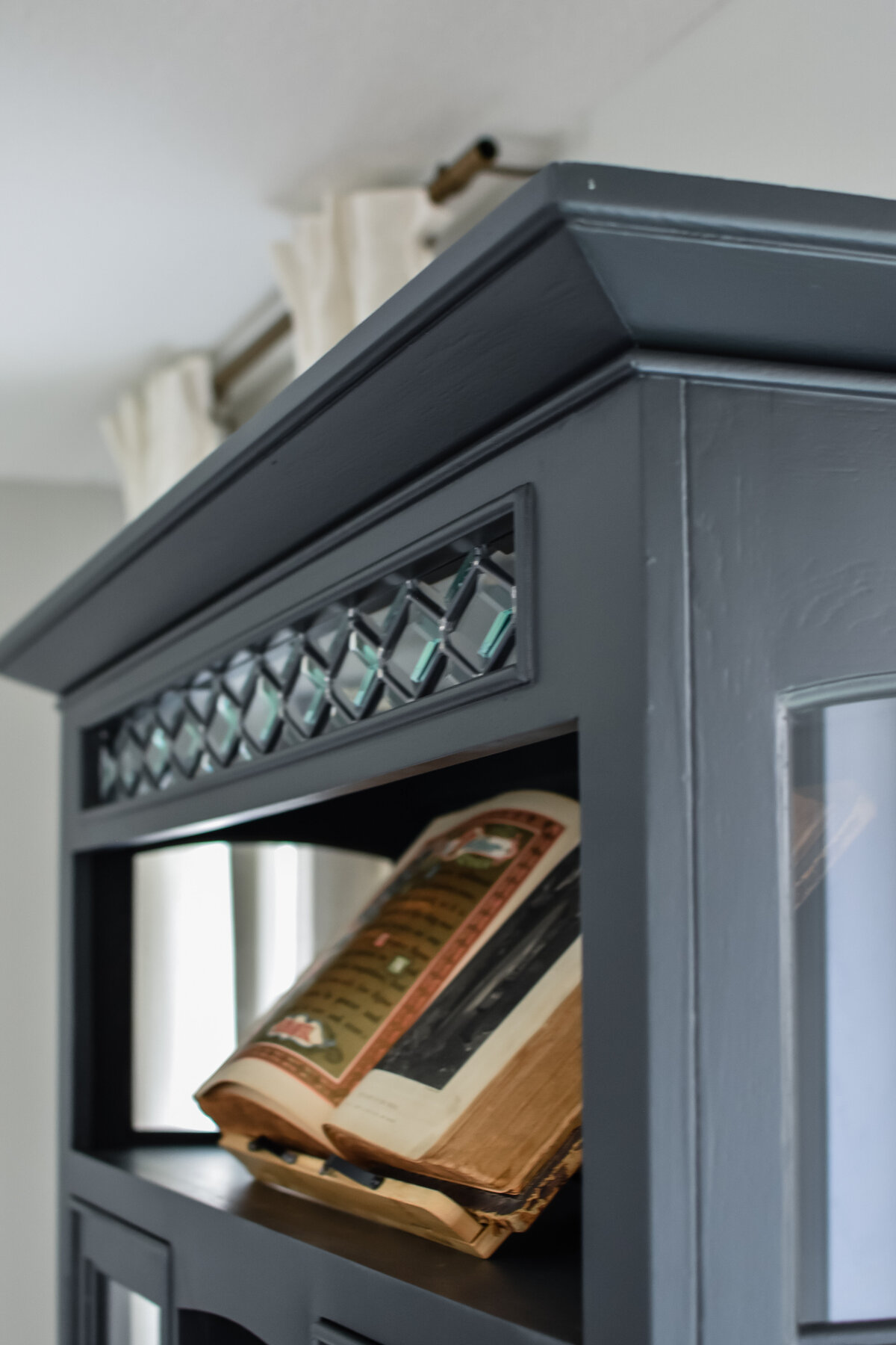 An old bible sits open on a book holder in a dining room hutch