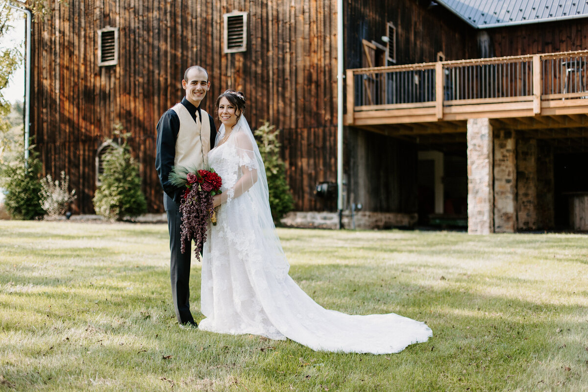 wedding couple standing in front of a rustic building smiling together